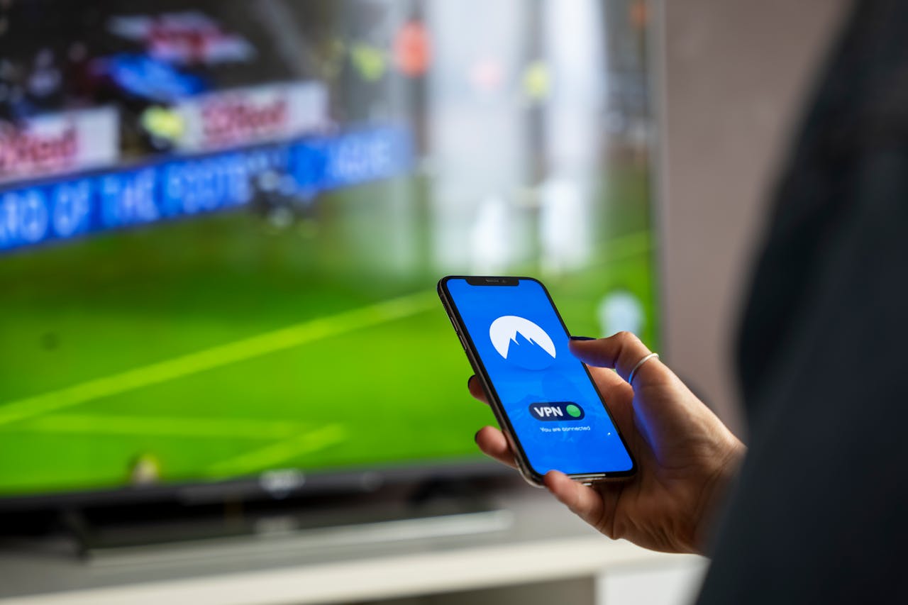 Mastering the First Impression: Your intriguing post title goes here Close-up of a person holding a smartphone with a VPN app, streaming sports on TV.